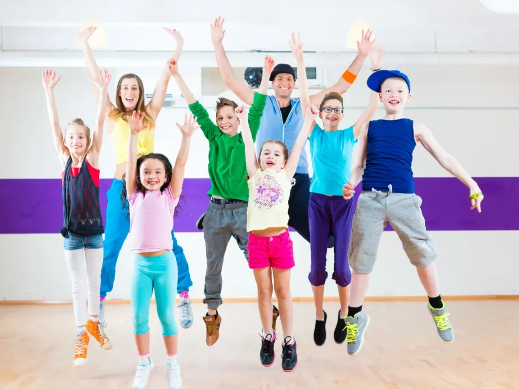 A mix of dancers (kids, teens, and adults) practicing together in a bright, modern studio.