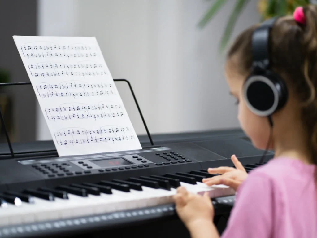 A young musician playing guitar or piano in a cozy, creative space with sheet music and headphones