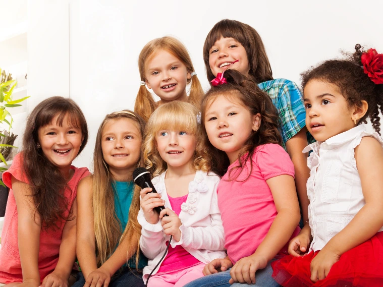 Group of happy children singing together and sharing a microphone during a kids’ music class, showing confidence, rhythm, and teamwork through music