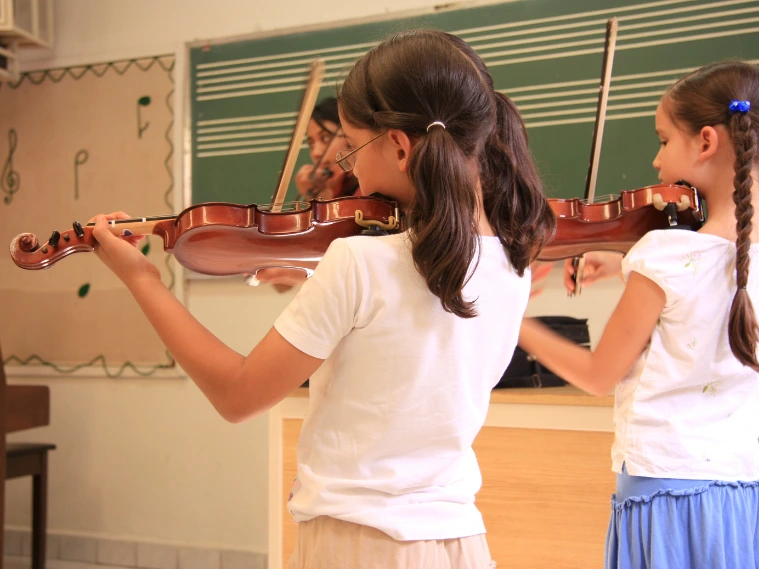 Two young girls practicing violin together in a music classroom