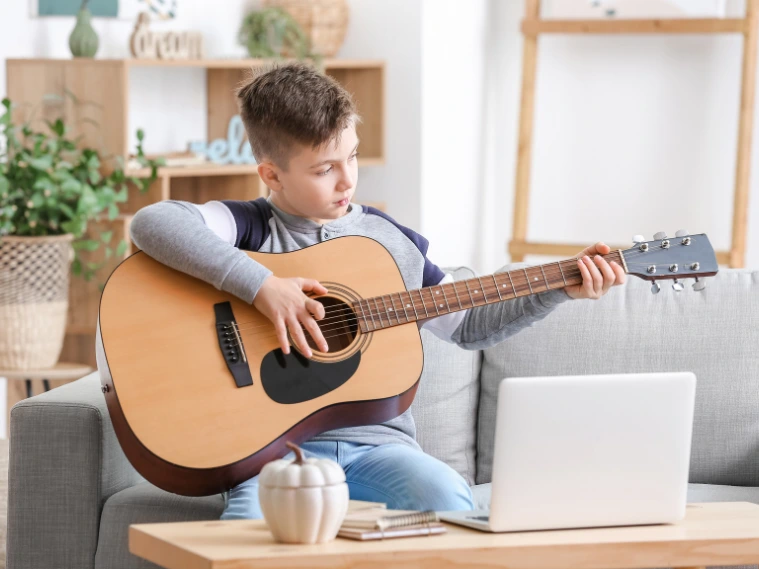 Kid in a virtual music lesson on a laptop screen, playing a guitar, highlighting online interactive learning.