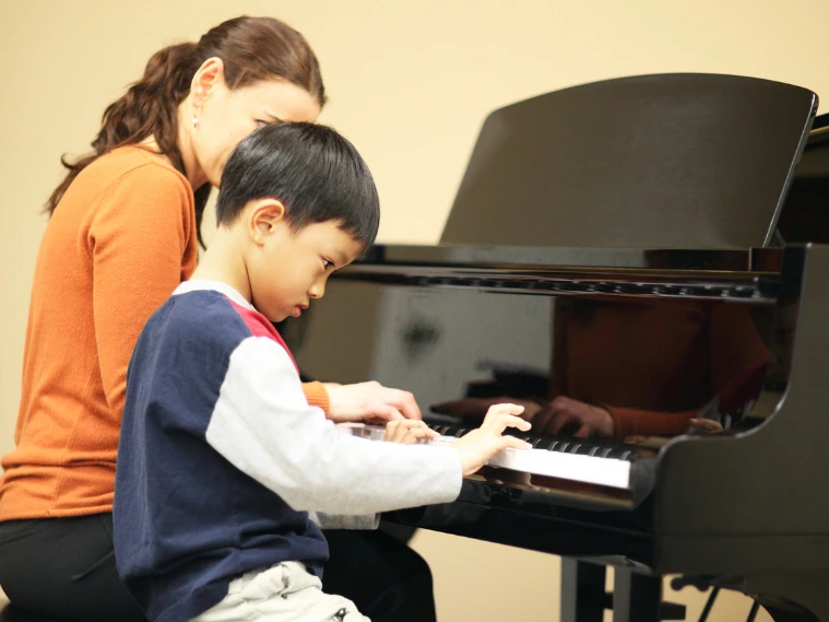 Child receiving one-on-one music instruction from a teacher, practicing piano in a focused and supportive environment