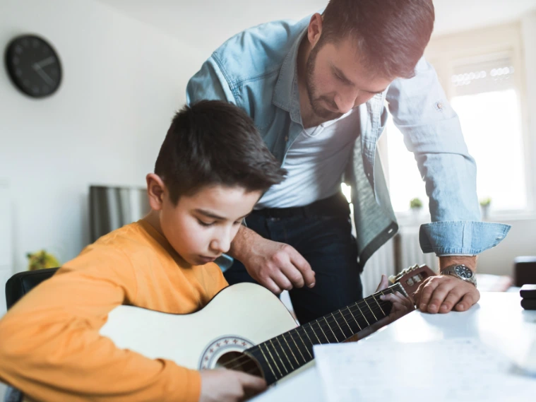 Young student playing guitar during a private music lesson, guided by an experienced instructor for personalized learning
