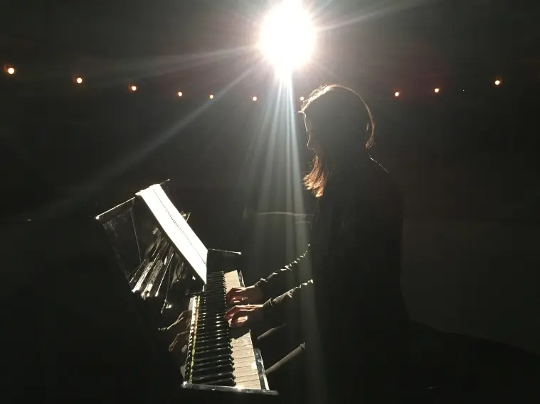 Black silhouette of a modern pianist seated at a grand piano, slightly angled sideways
