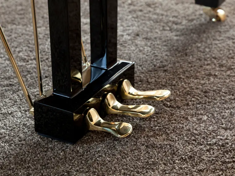 Close-up of piano pedals showing sustain, soft, and sostenuto pedals on an acoustic piano