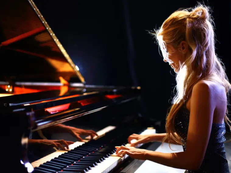 Concert pianist performing on a grand piano under stage lights during a classical recital