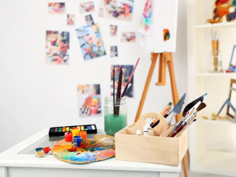 Art studio workspace with mixed media tools, including paper, fabric, paint, and creative supplies arranged on a table.