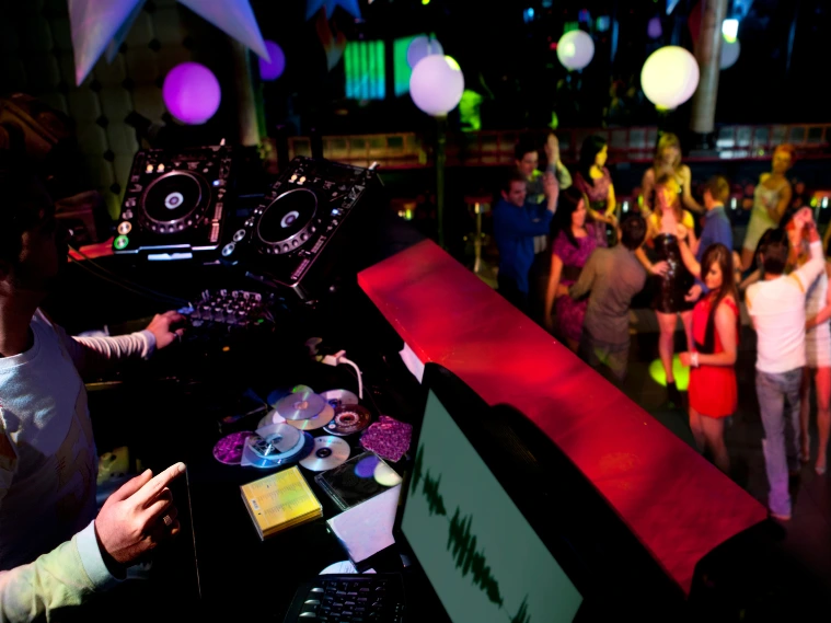 DJ mixing music with crowd dancing in the background at a lively event