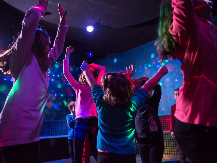 Group of friends dancing at a party with colorful lights and energetic atmosphere