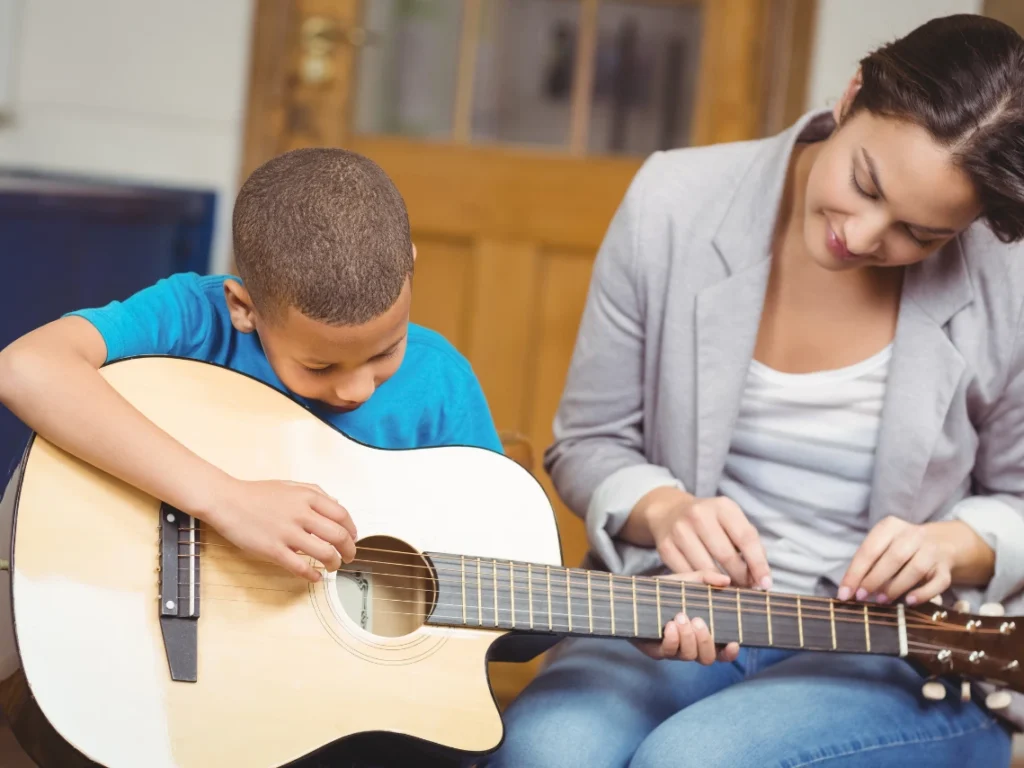 Guitar teacher guiding a beginner through finger placement and chord transitions in a beginner guitar class in Gilbert, Arizona.