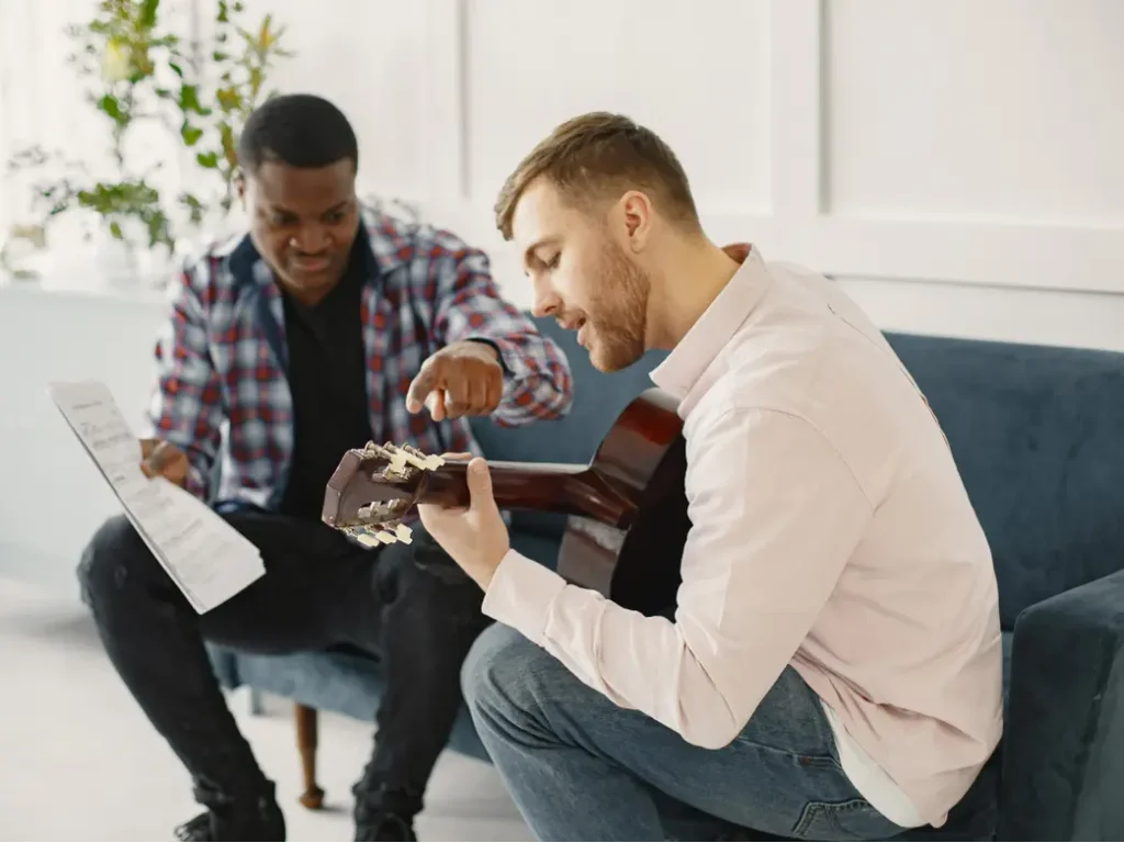 Adult student learning to play guitar with an instructor while following sheet music during a private music lesson