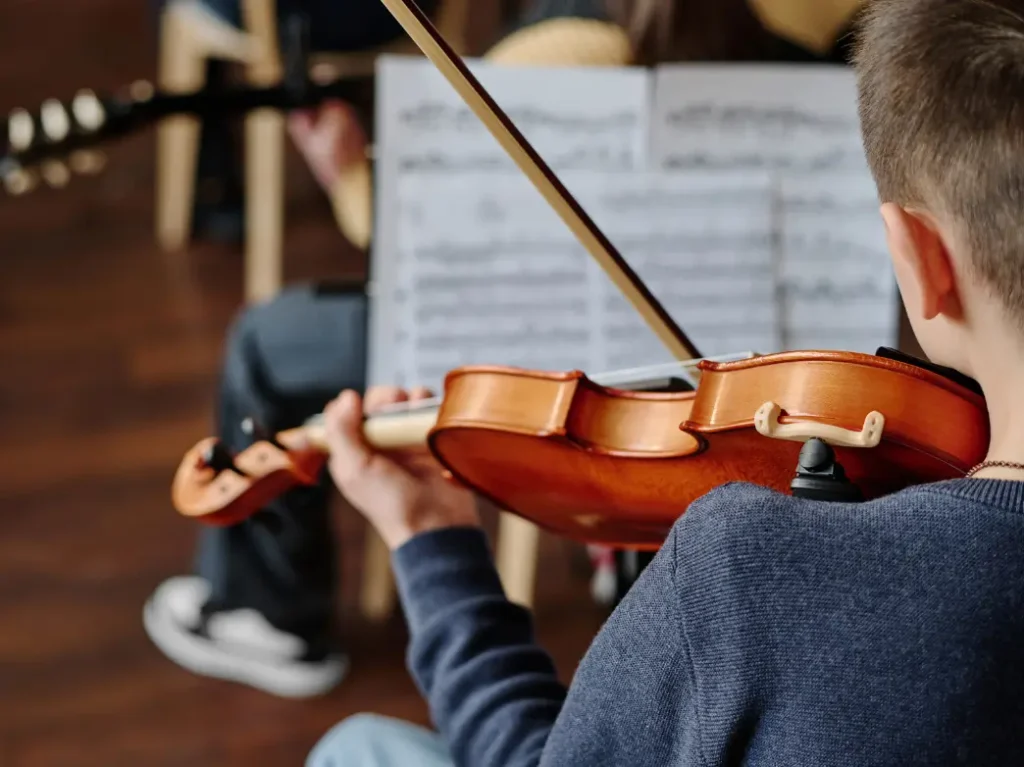Boy practicing violin during a music lesson while reading sheet music in a classroom