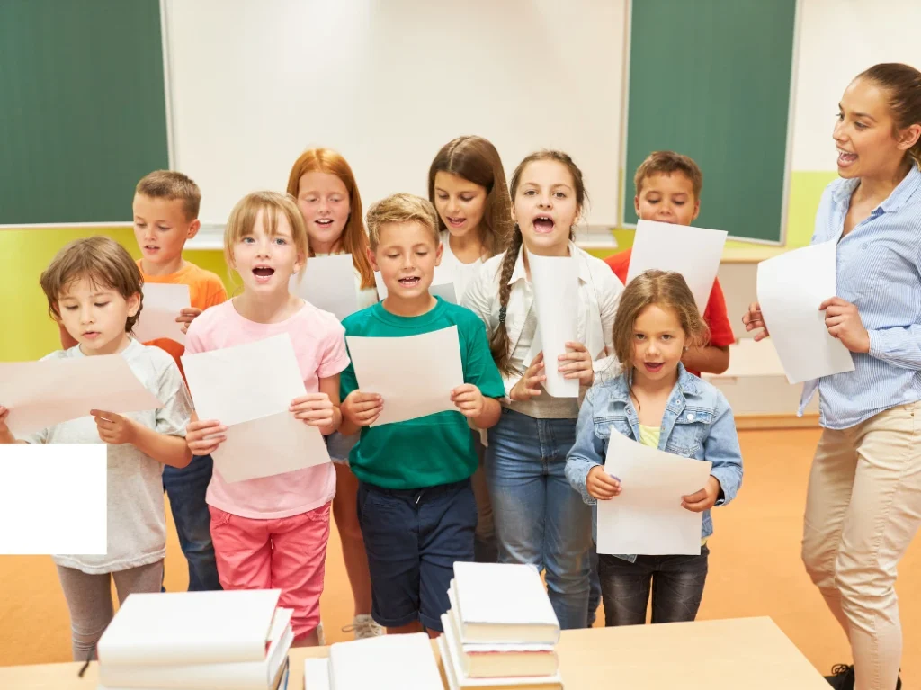 Children participating in a group vocal lesson, singing together while following sheet music with guidance from their instructor.