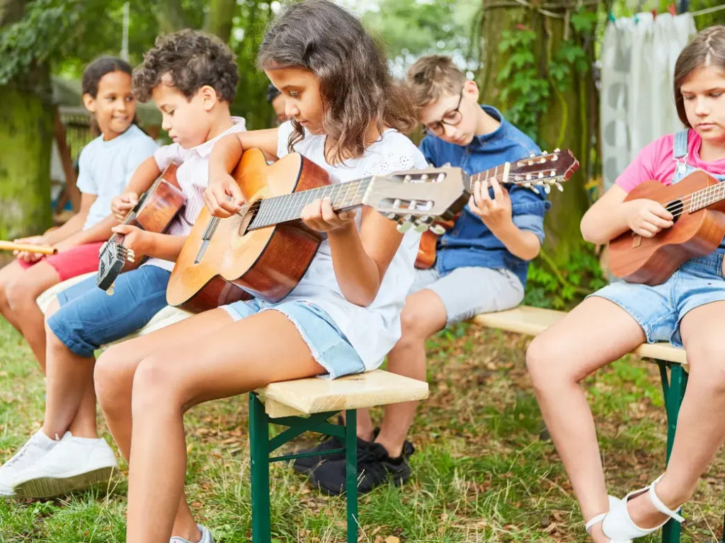 Children practicing guitar and ukulele together during an outdoor group music lesson