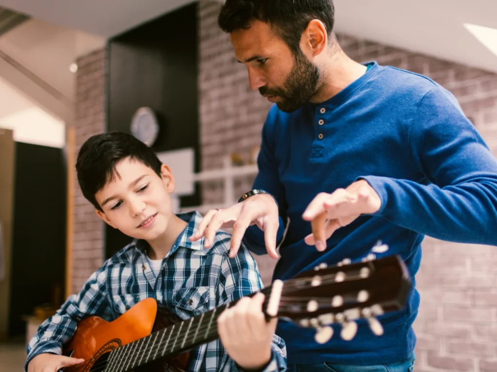 Young student learning to play guitar with guidance from a music instructor during a beginner guitar lesson