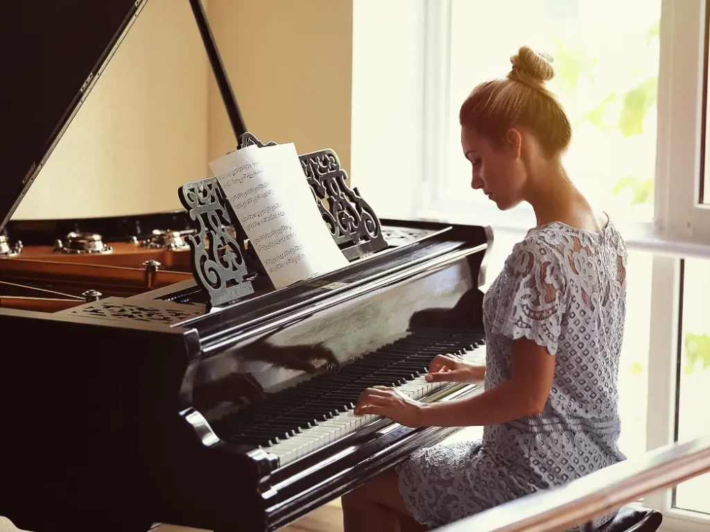 Adult student practicing piano while reading sheet music at a grand piano.