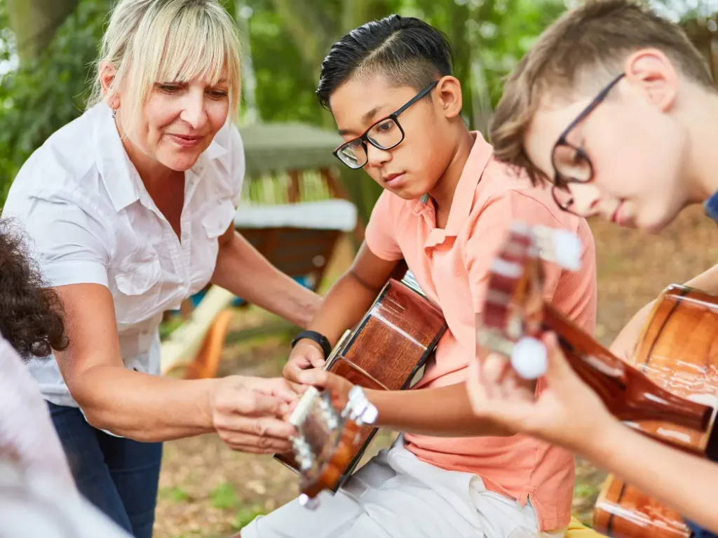 Children learning acoustic guitar with guidance from an instructor during a group guitar lesson