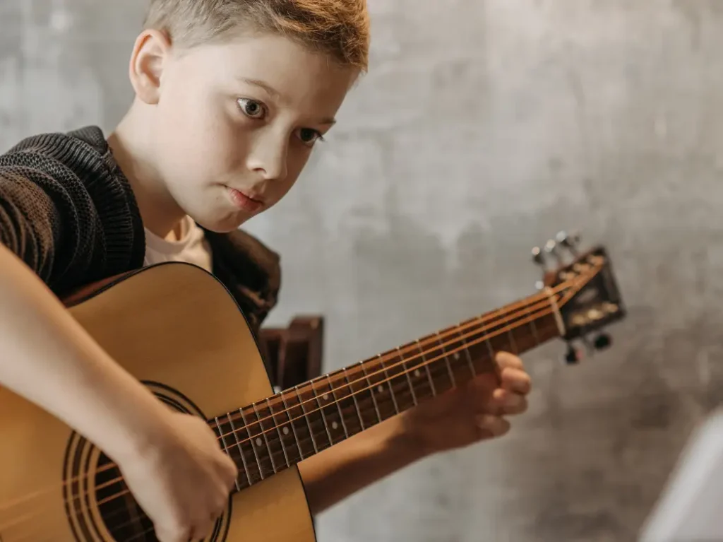 Student practicing acoustic guitar with guidance from an instructor during a guitar lesson