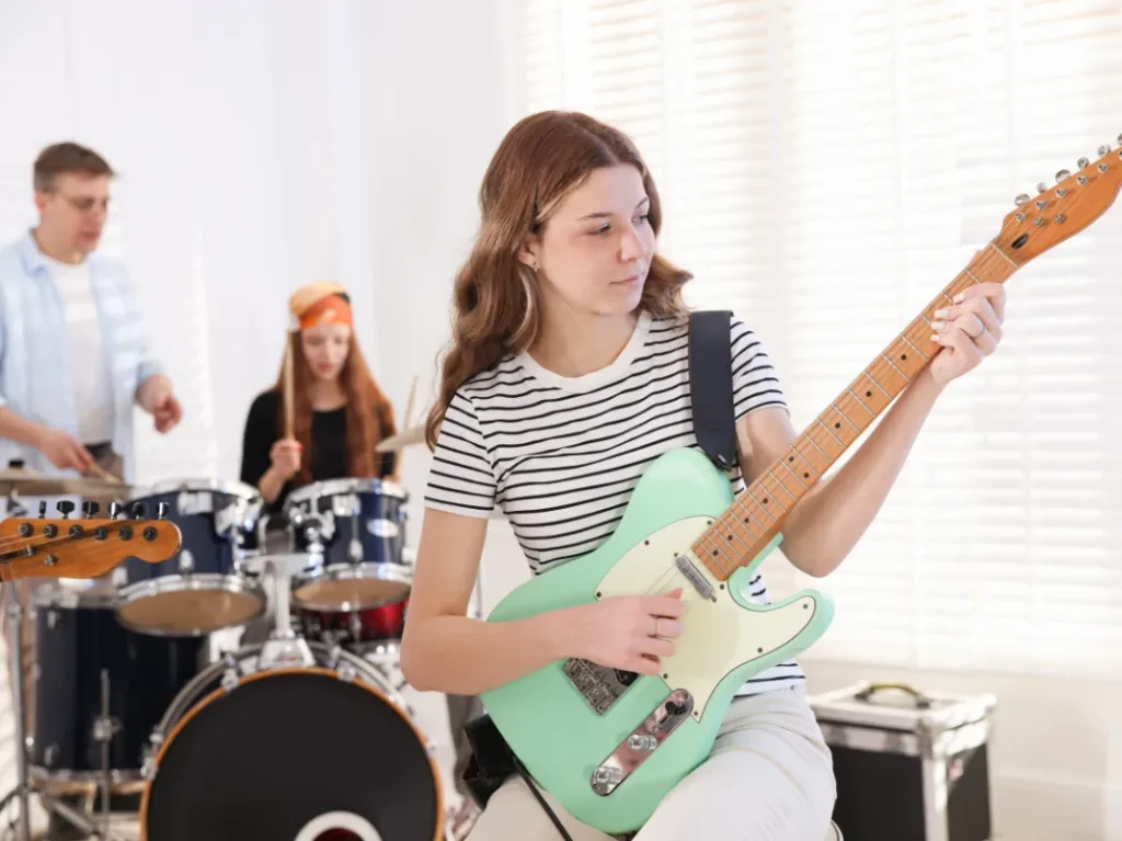 Teen student practicing electric guitar with a drummer during a group music class.