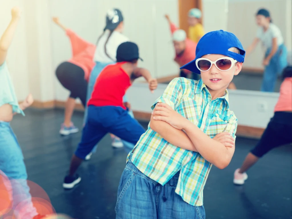 Young boy posing confidently during a kids’ hip-hop dance class with other students dancing in the background.